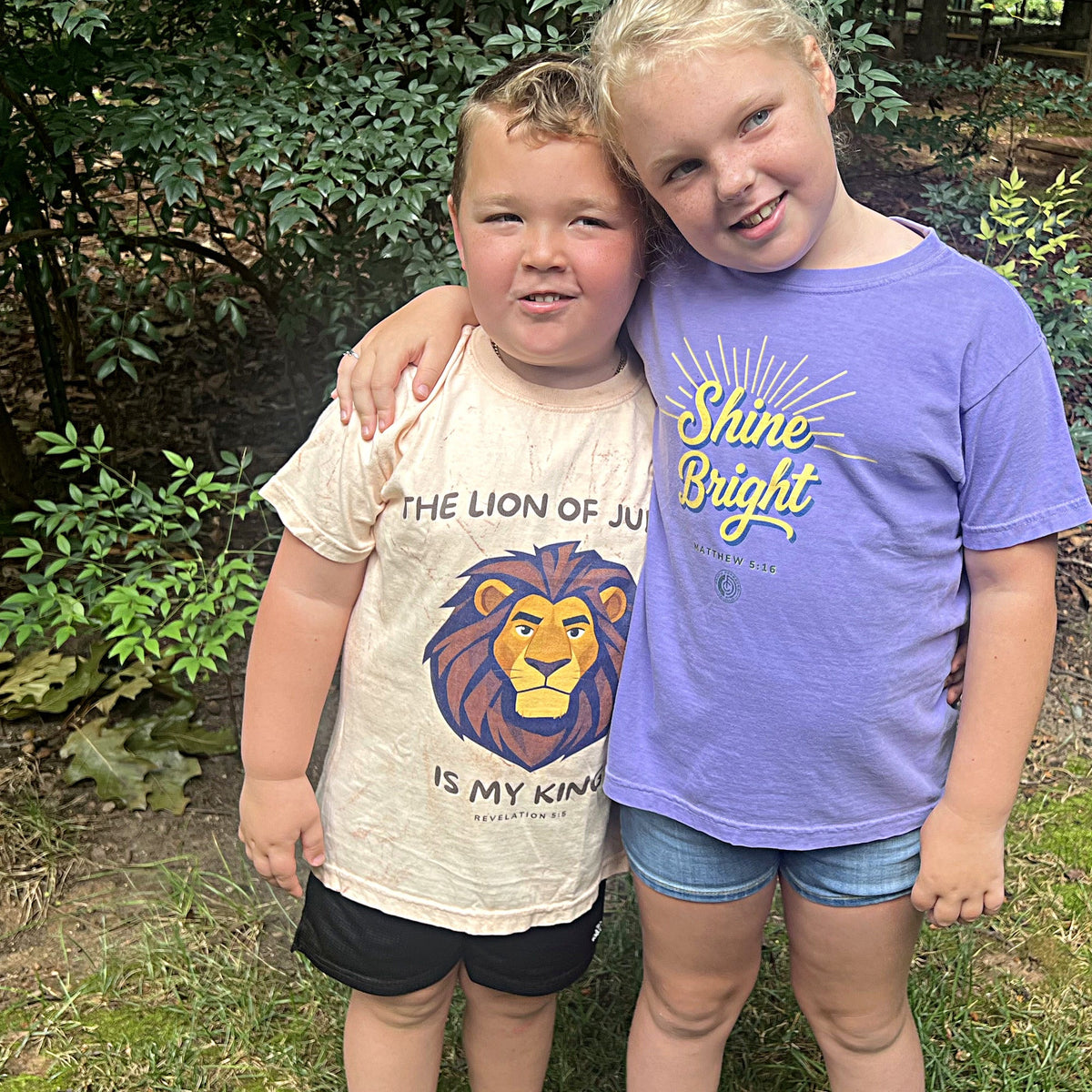 Two children wearing The Lion of Judah Is My King and Shine Bright youth tees